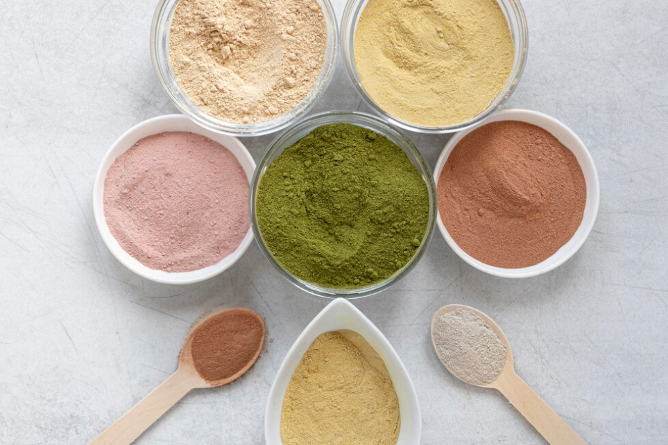 colorful green, pink, orange, and gray protein powders in bowls and spoons