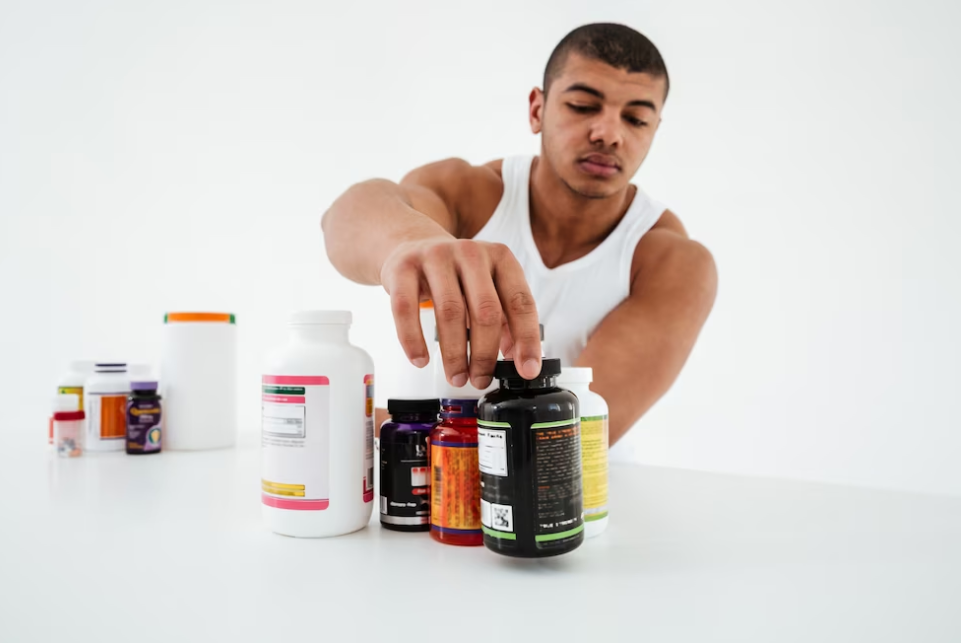 man in a white t-shirt picking a bottle of protein pills among all the bottles on the table