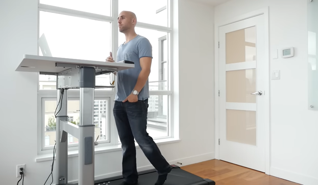 man in a blue t-shirt an jeans on desk treadmill in his room
