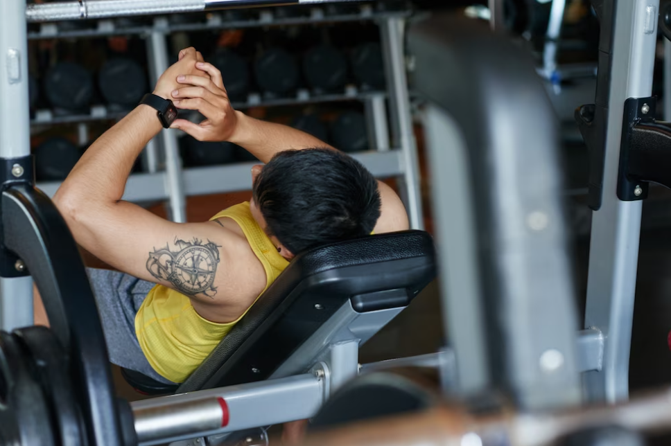 tattooed man reclining on a bench in the gym and looking at smartwatch