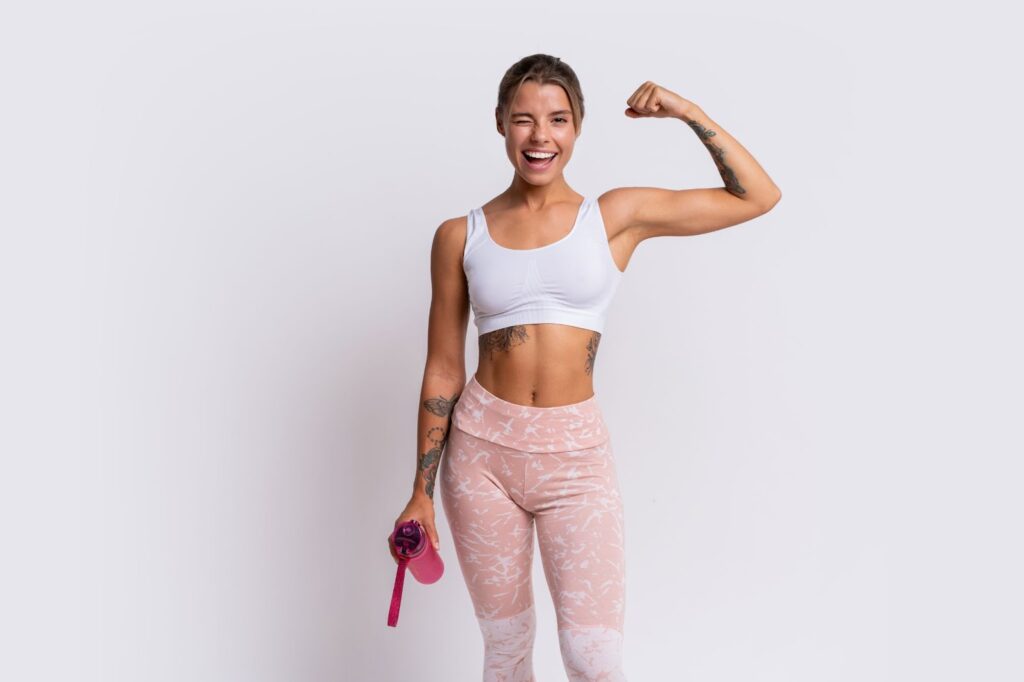 The athletic woman shows off her muscles and holds a bottle