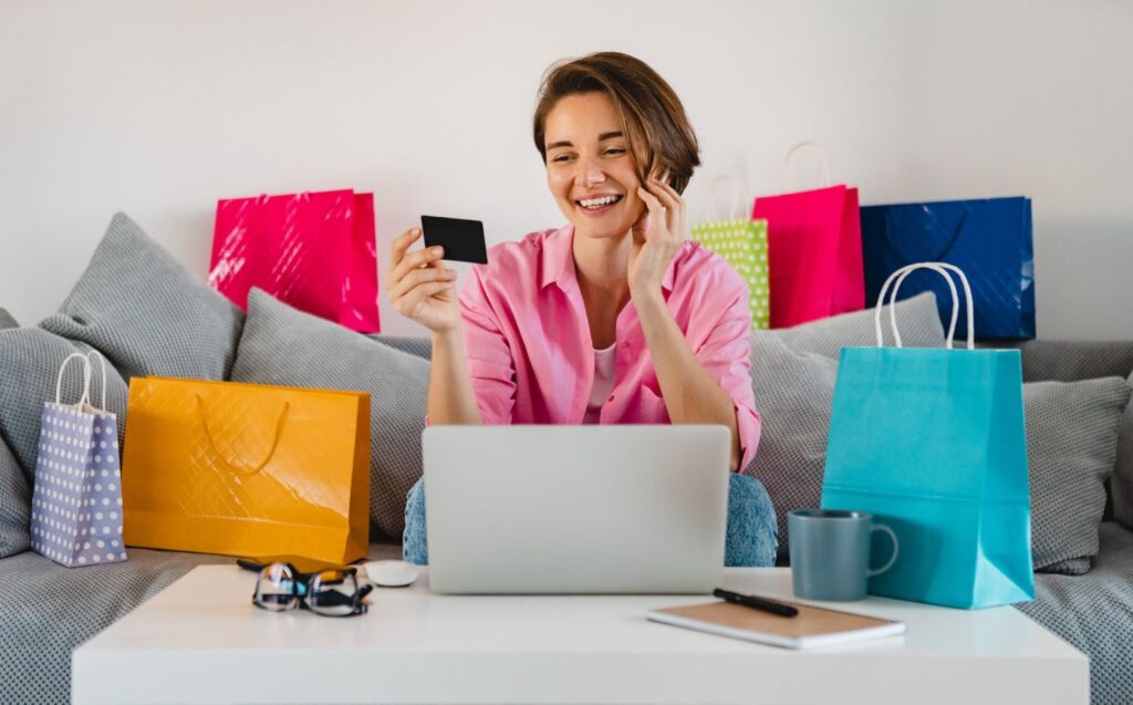 Happy woman in pink shirt sitting among colorful shopping bags holding credit card